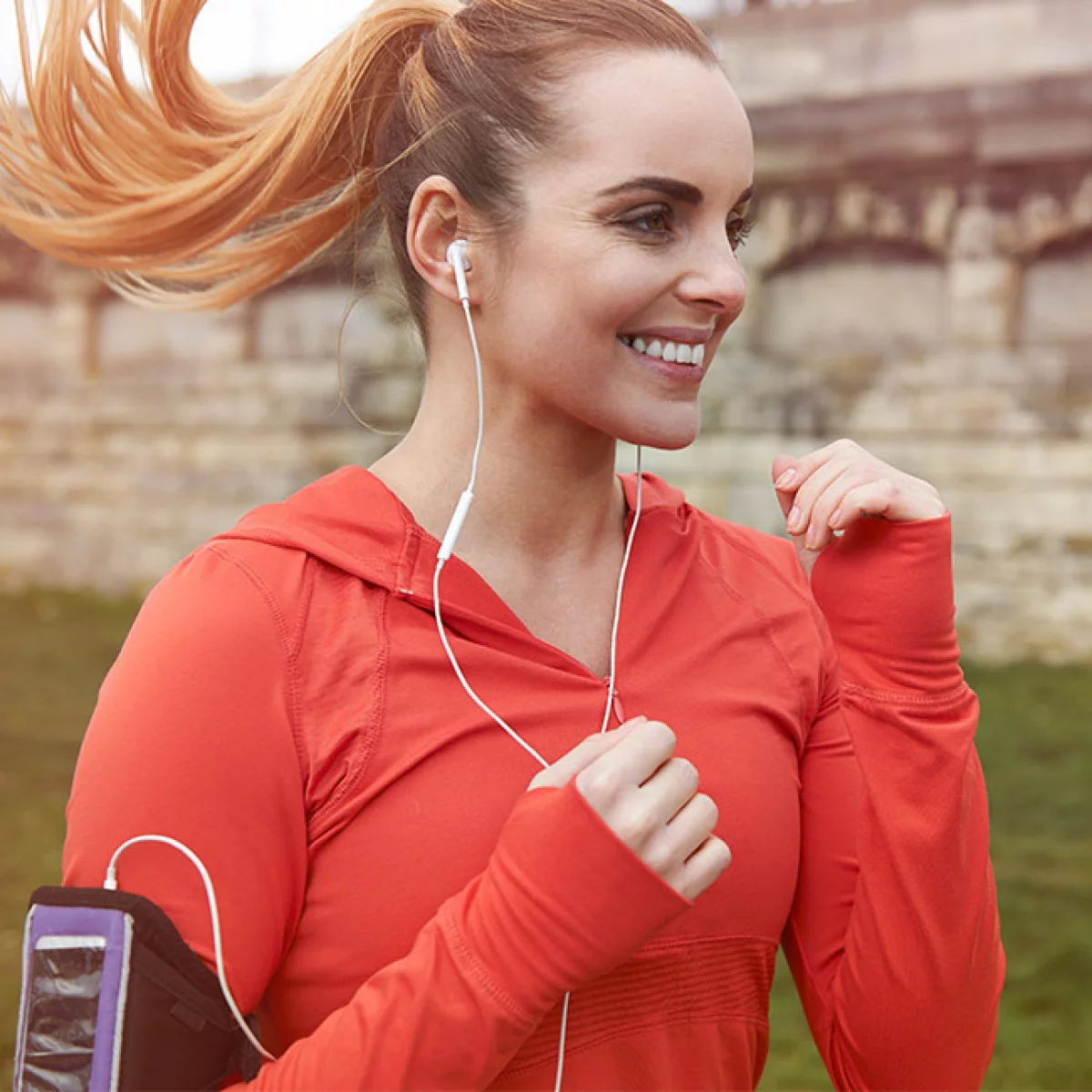 Frau joggt mit weißen Kopfhörern und rotem Sportoutfit im Freien