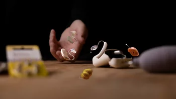 Verschiedene Hörgeräte und Zubehör auf Holztisch mit Hand im Hintergrund