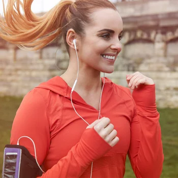 Frau joggt mit weißen Kopfhörern und rotem Sportoutfit im Freien